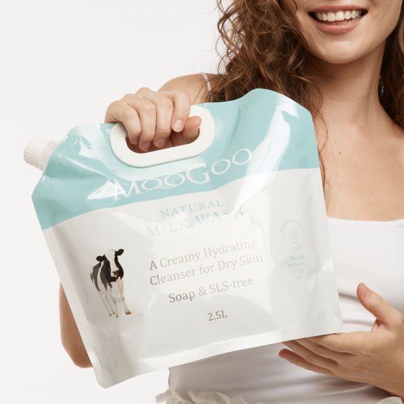 Smiling curly haired model holding MooGoo Milk Wash 2.5L pouch with one hand on handle and the other underneath, 