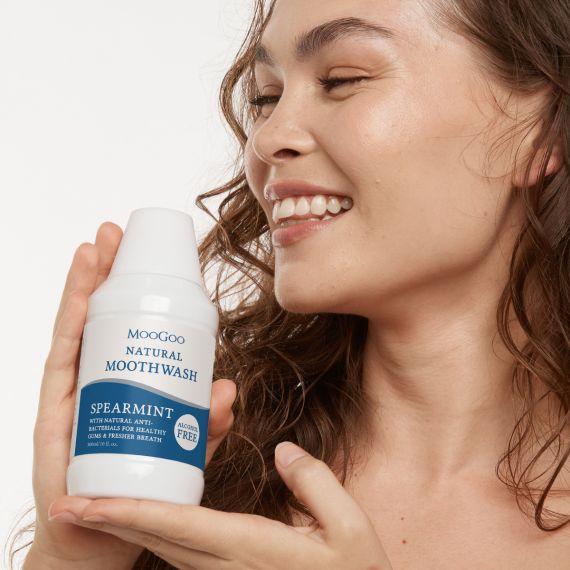 Female model with brunette curly hair holding the MooGoo Natural Moothwash with Natural Anti-Bacterials for Healthy Gums & Fresher Breath