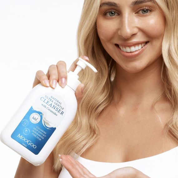 Blonde lady smiling holding MooGoo Ultra Gentle Cleanser with Ceramides on white background