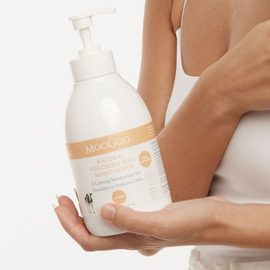 Olive skinned female model in white singlet top holding the MooGoo Natural Soothing MSM Moisturiser 500g bottle with pump top in her hand. 