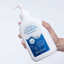 Women's hand holding MooGoo Ultra Gentle Cleanser with Ceramides on white background